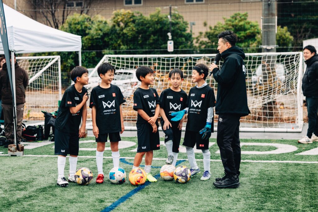 人工芝グラウンドに整列する少年チームと指導者