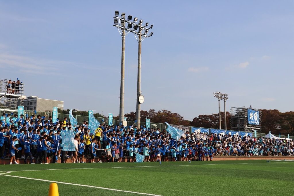スタジアムのスタンドに集まる青いユニフォームの子どもたち