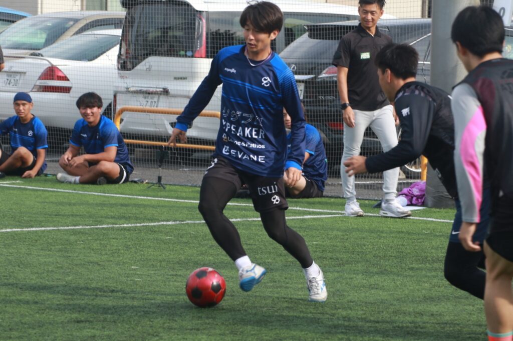 コーチの指導のもとフットサルコートでドリブル練習する選手
