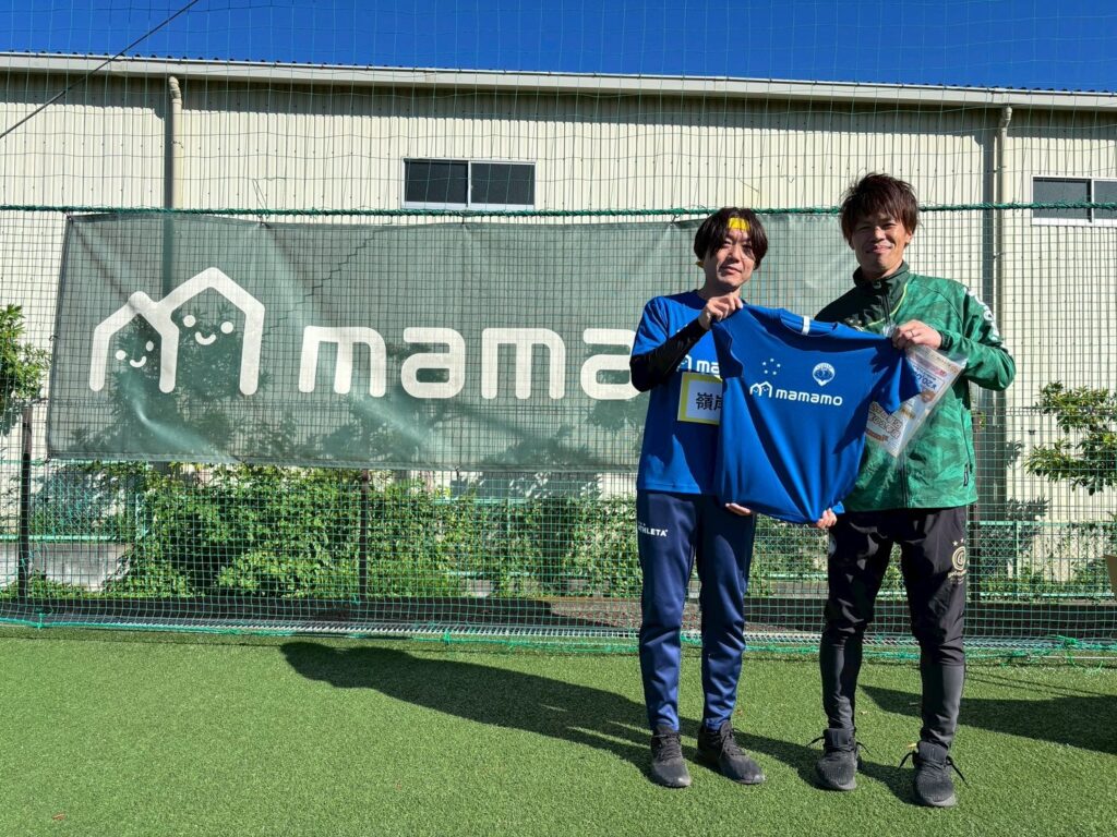 紺色のジャケットを手にする2人と企業ロゴの横断幕