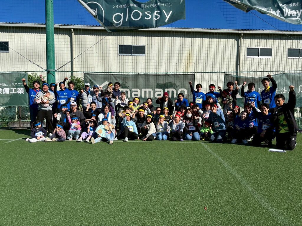 人工芝ピッチに集合した大人数の記念写真（企業ロゴ横断幕）