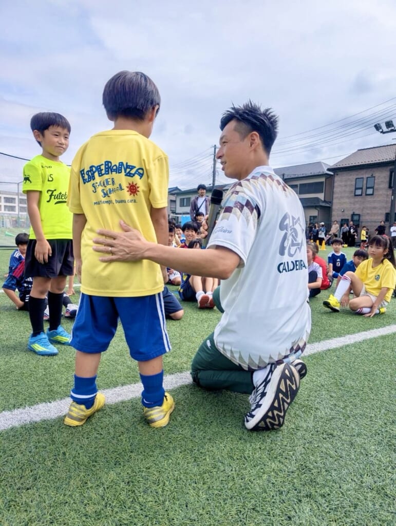 人工芝のグラウンドで子どもに歩み寄り、マイクを向けて話を聞くMCおのしん
