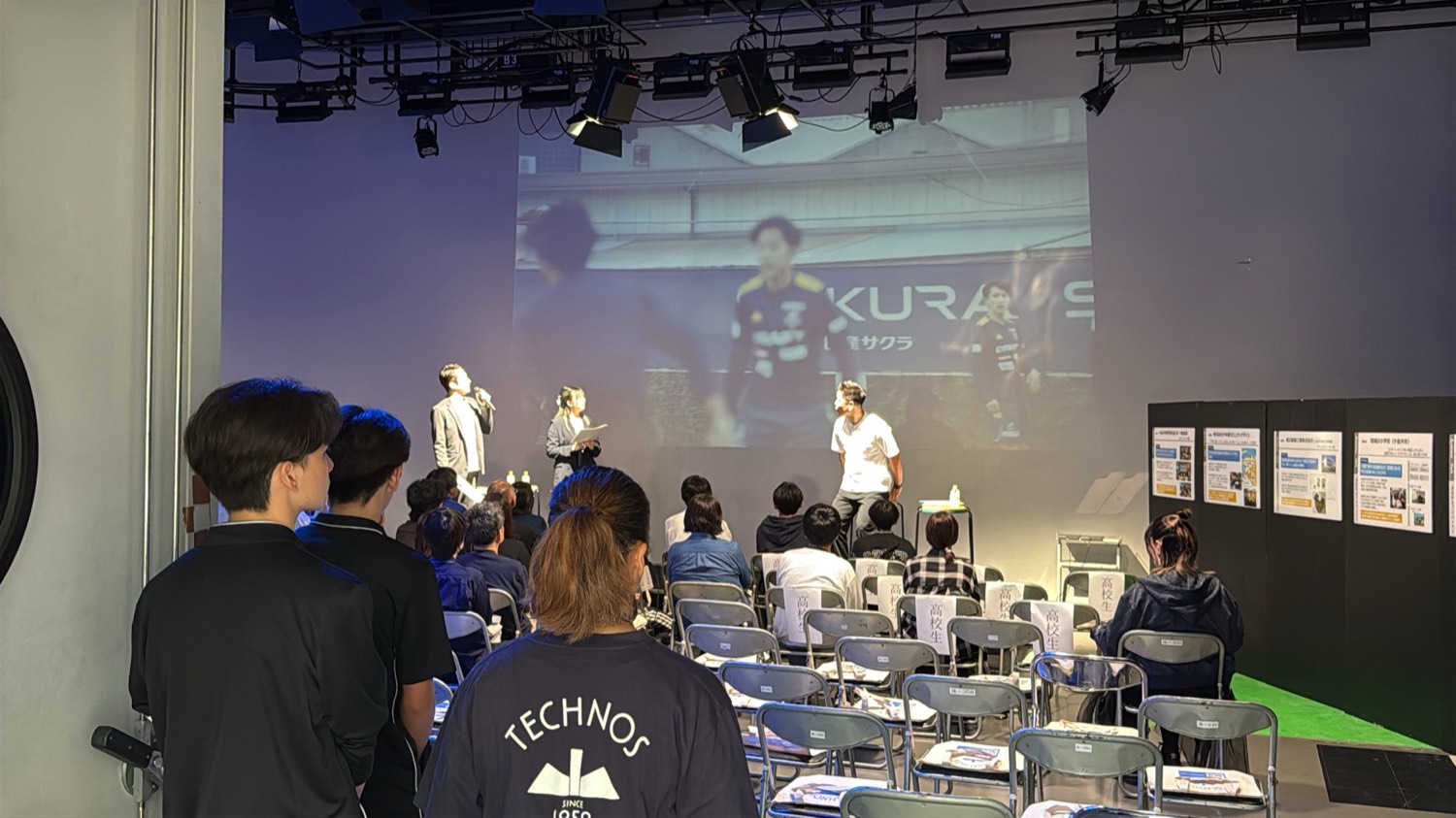 スクリーンの前でトークショーを進行する登壇者と、客席で聞く高校生たち