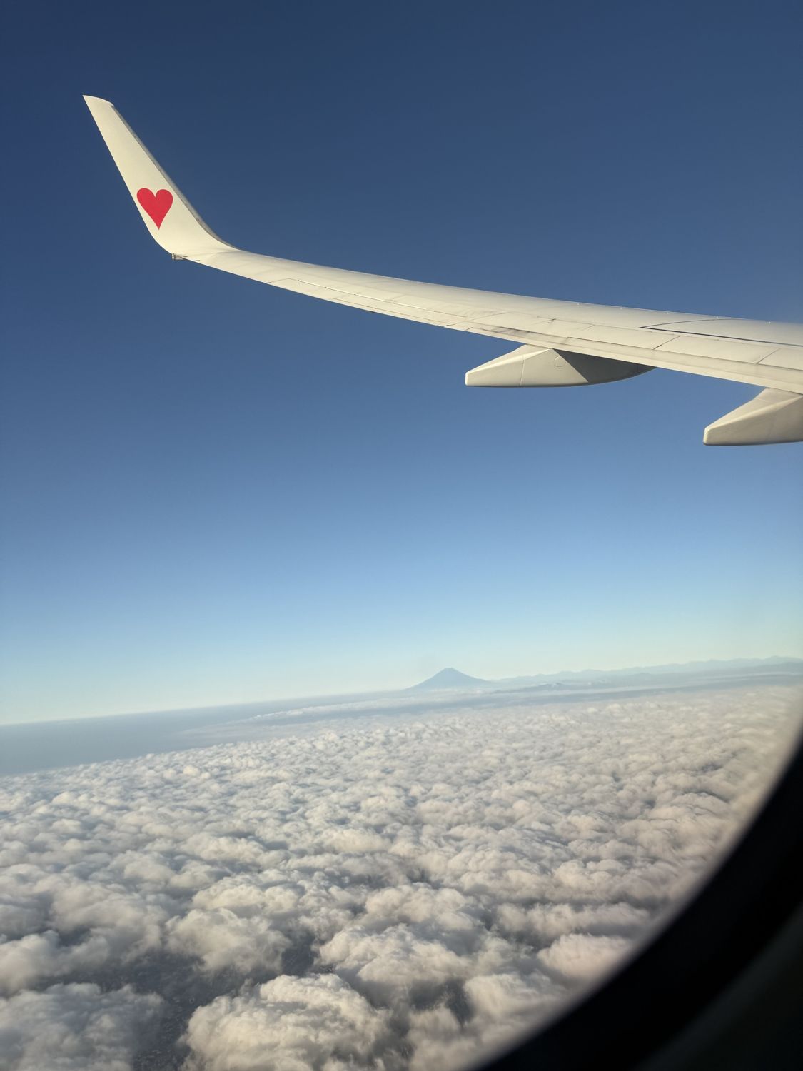 飛行機の窓から見た、主翼と雲海の向こうの富士山